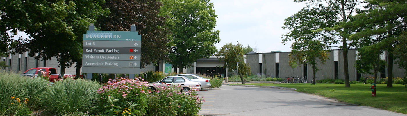 Blackburn Hall building with pink flowers in the foreground and a few cars in the parking lot