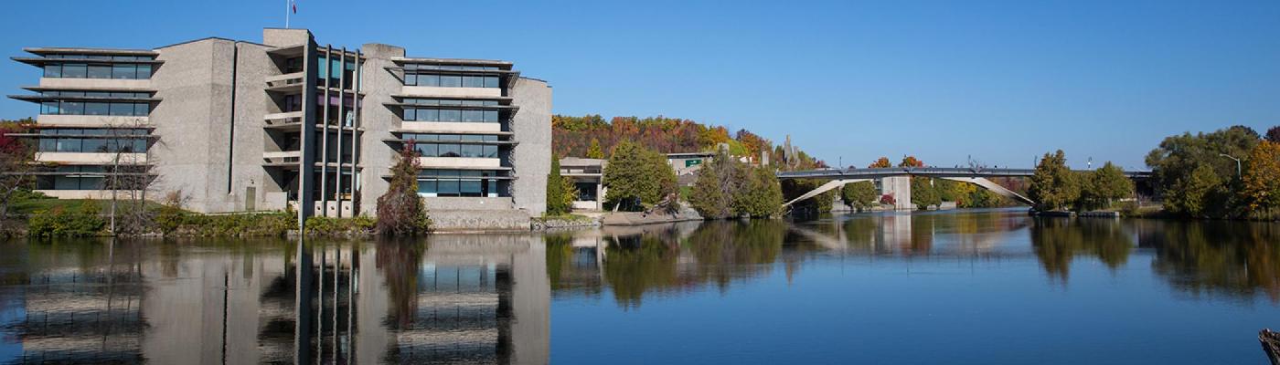 Exterior view of the Bata library and the Faryon bridge in the fall sun from across the otonabee river, looking North