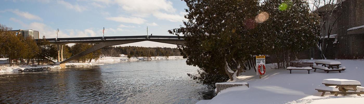 Exterior view of the Faryon bridge in the winter snow and sun from the Champlain College bank of the Otonabee river