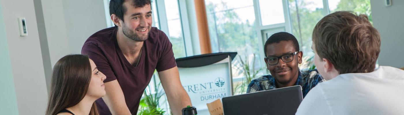 4 students sitting at a round table in the foyer of the Durham campus in front of laptops