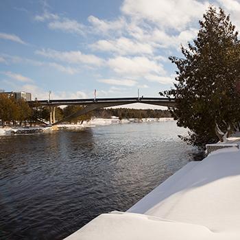 Exterior view of the Faryon bridge in the winter snow and sun from the Champlain College bank of the Otonabee river