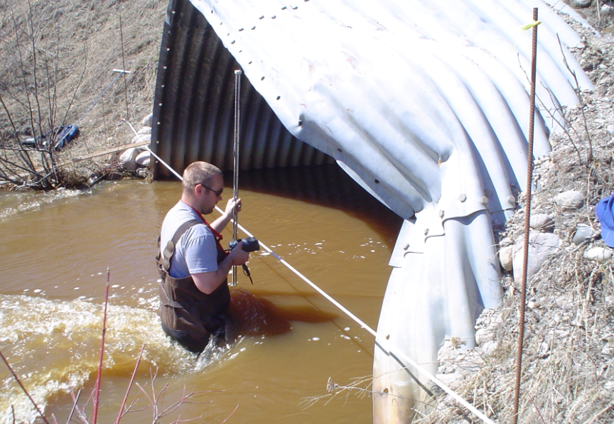 male wearing hip waders in creek measuring water levels