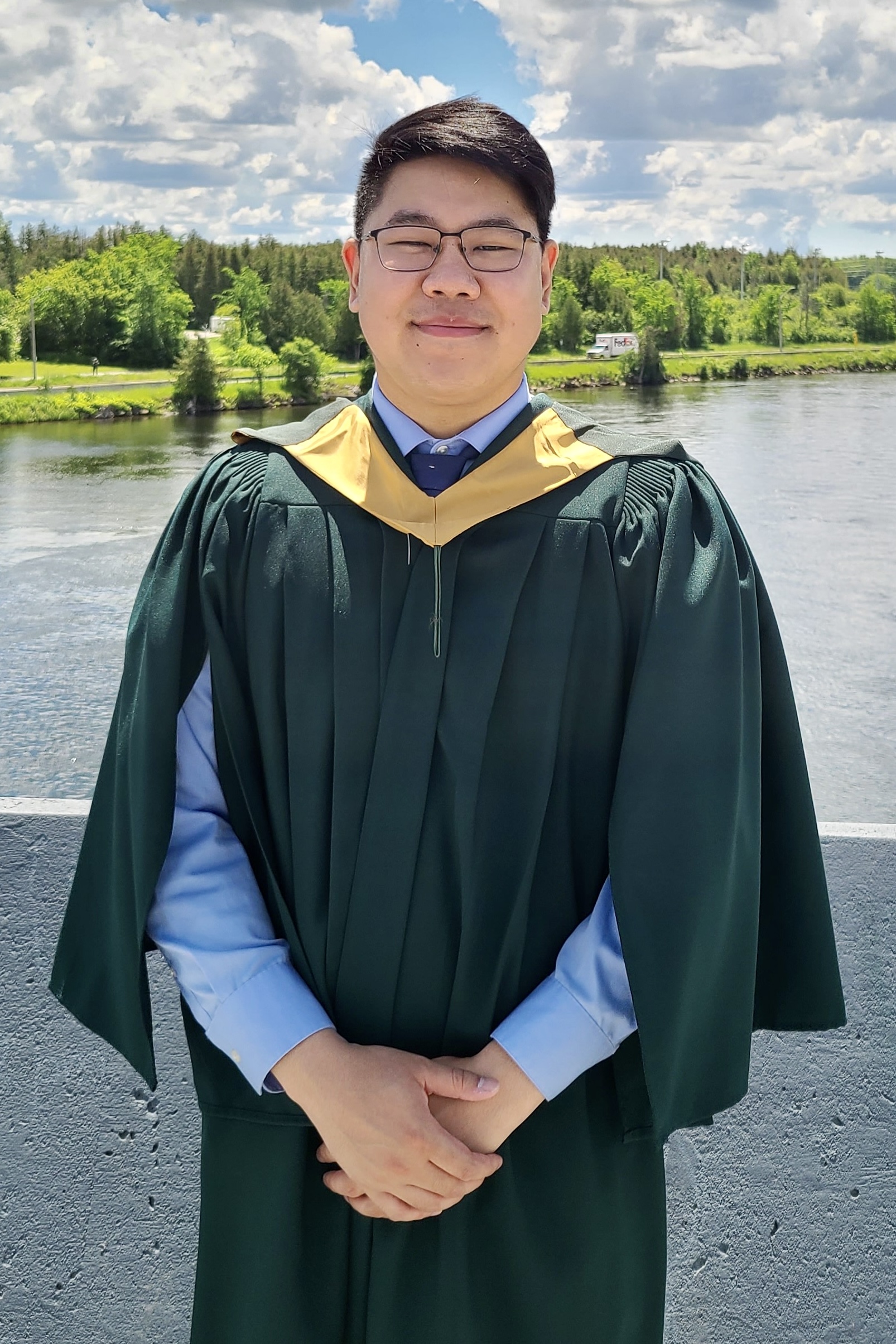 smiling graduate with blue sky, white clouds and water in background