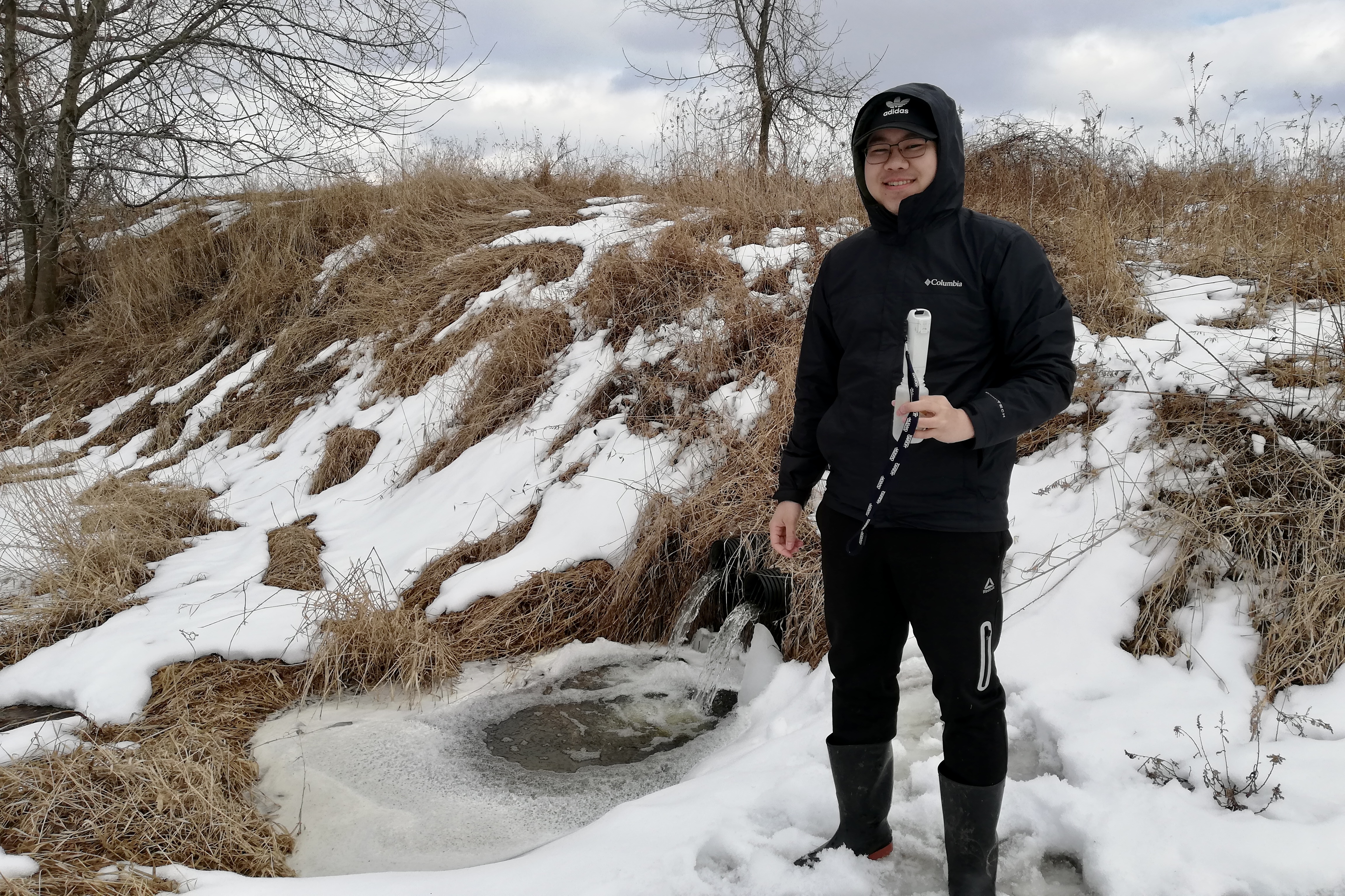 smiling man in black clothing standing in snow, holding test tube