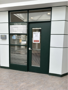 A white hallway with a green door, signs read Counselling Services, suite 113
